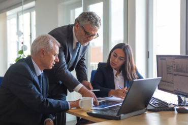 Concentrated colleagues watching statistic charts and talking about work. Professional senior managers and young assistant preparing business plan. Teamwork, management and partnership concept