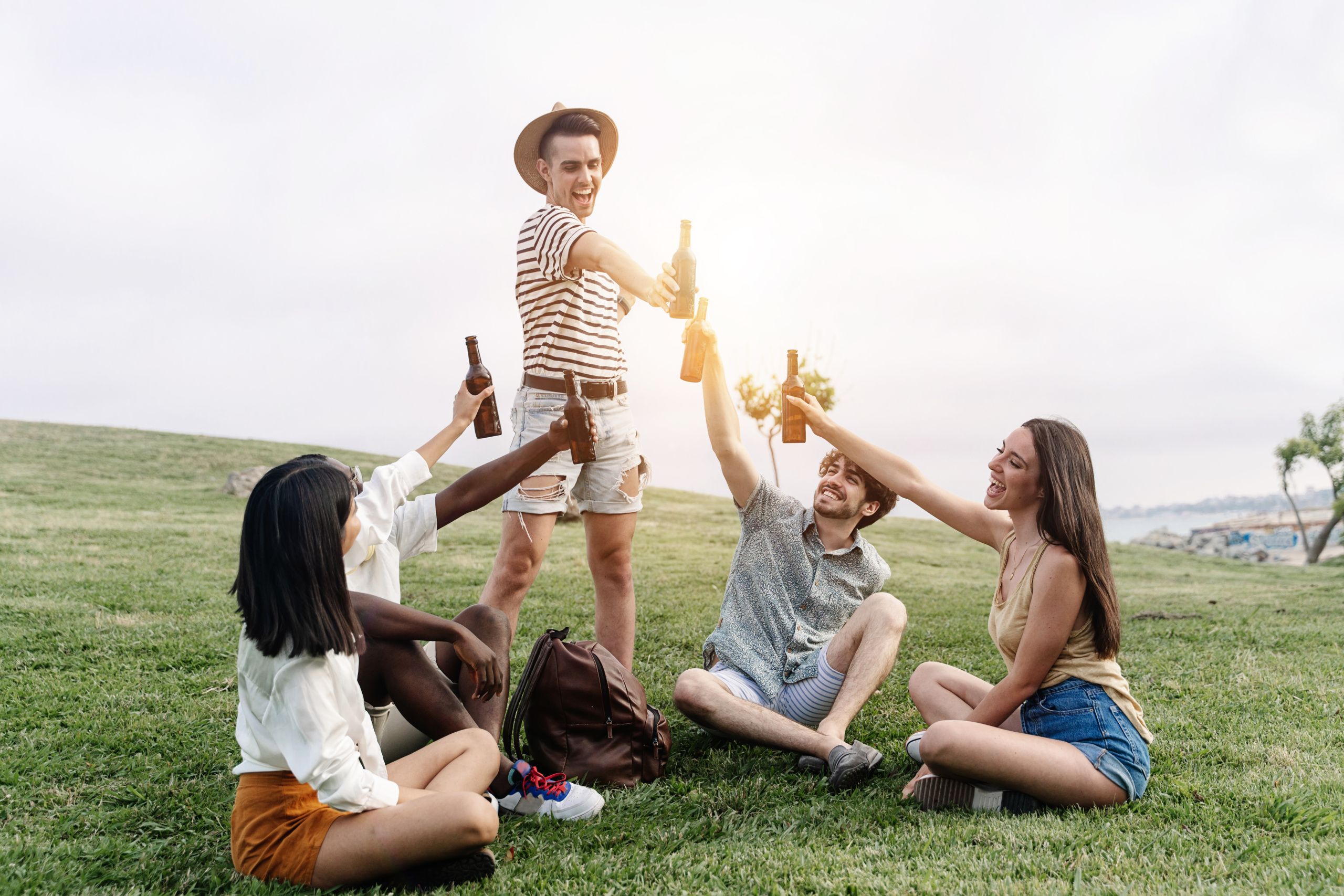 Friends toasting beer in public park to celebrate summer vacations and friendship